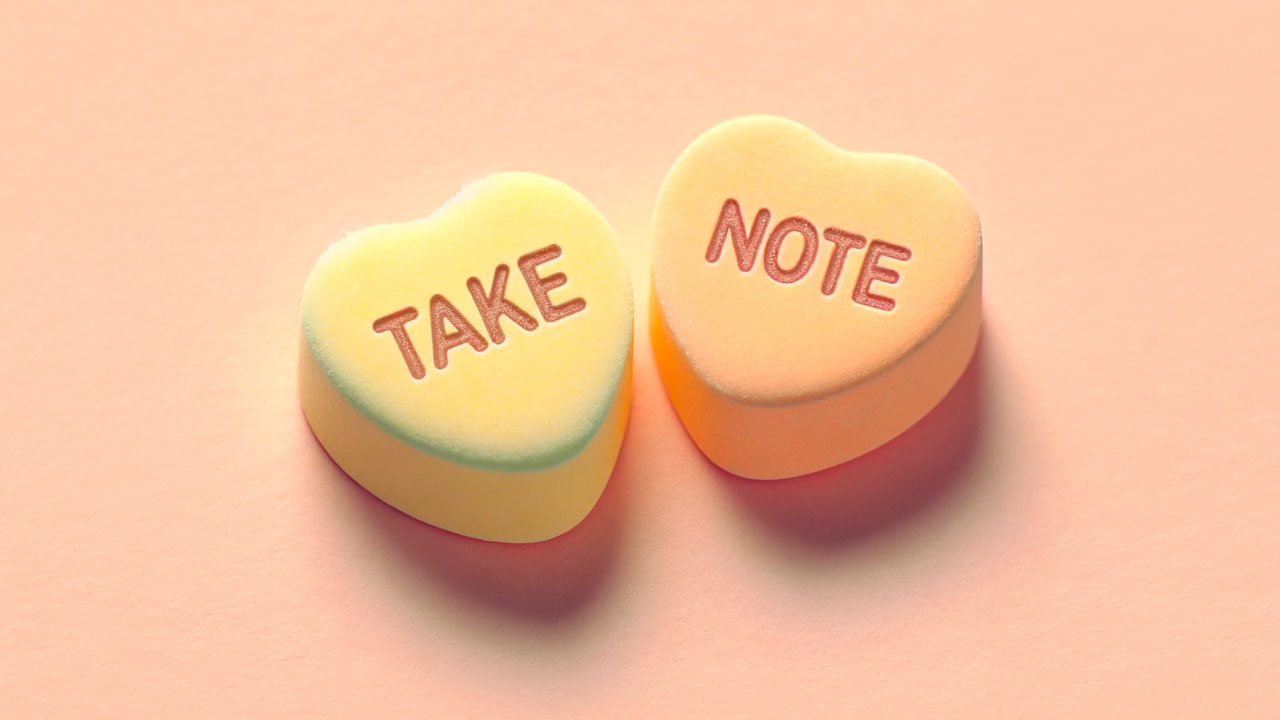 Two pastel-colored Valentine’s Day candy hearts with the words Take and Note.